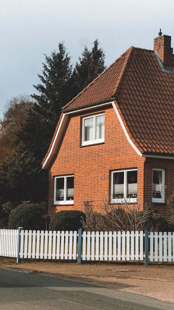 A cozy red brick house with a white picket fence under a clear sky.